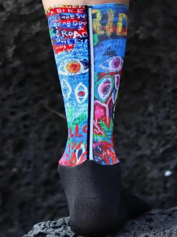 Colorful cycling socks with eye and text graphics, worn on rocky terrain for outdoor rides.