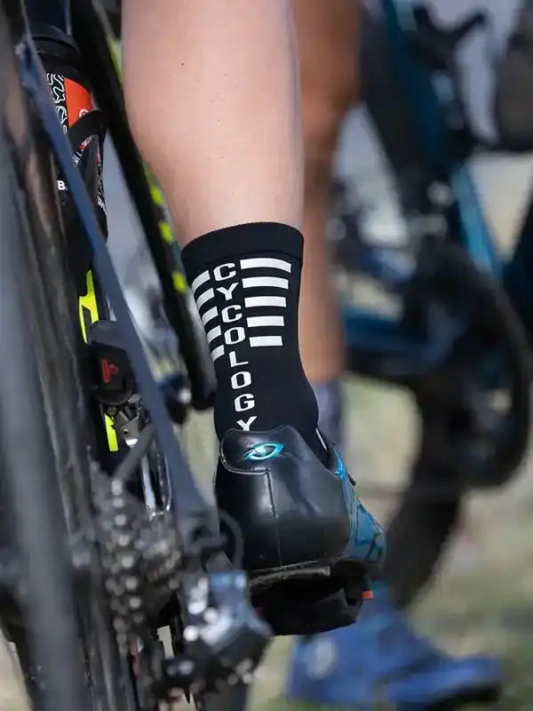Cycling socks with CYCOLOGY logo, worn with bike shoes on a road bike, ideal for men's and women's cycling gear.