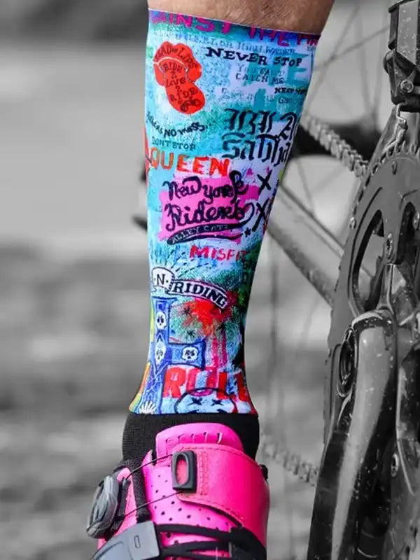 Colorful graphic cycling socks with bold text designs, worn with pink bike shoes and next to bike chain