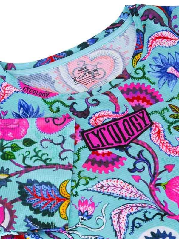 Cycology women's cycling jersey with vibrant floral print and pink logo patch on teal fabric