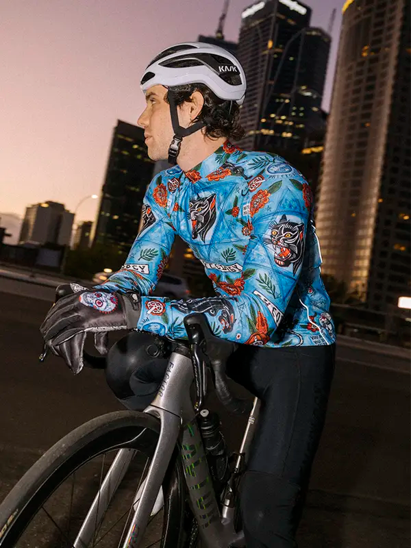 Cyclist wearing a Blue men's Winter  long sleeve cycling jersey with floral and panther design with a cityscape background