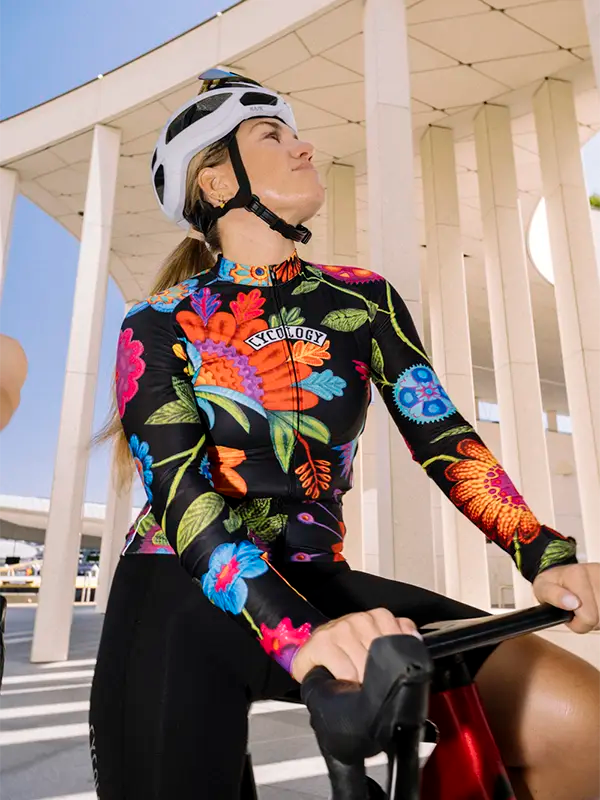 Person wearing a Colorful floral-patterned long sleeve cycling jersey on a black background with a helmet, sitting on a bicycle.