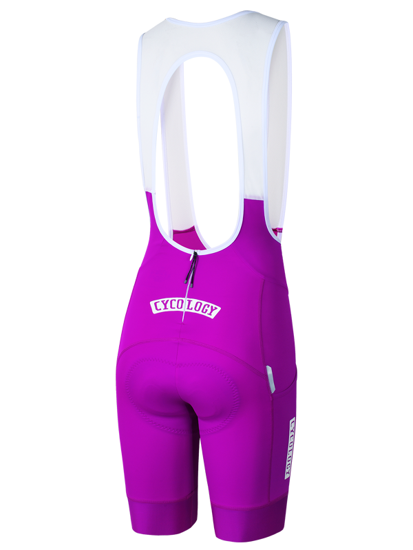 A pair of cycling bib shorts in vibrant magenta purple with a white upper bib panel and white printed text reading 'CYCOLOGY' on the back near rear  zipper shown against a plain white background.