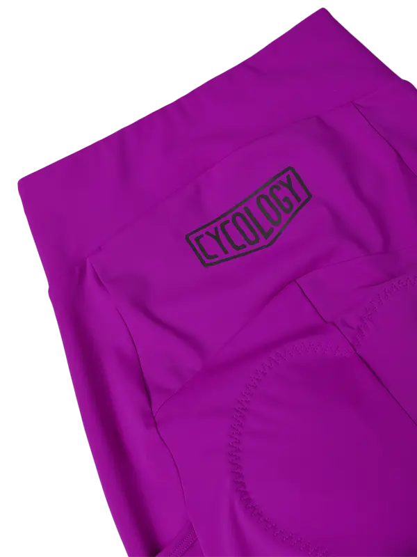 Purple high-waisted cycling shorts with a side cargo pocket a vertical black 'CYCOLGY' logo on the back shown against a plain white background.
