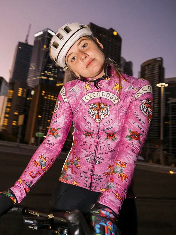 Person wearing a pink long sleeve cycling jersey with a cityscape background