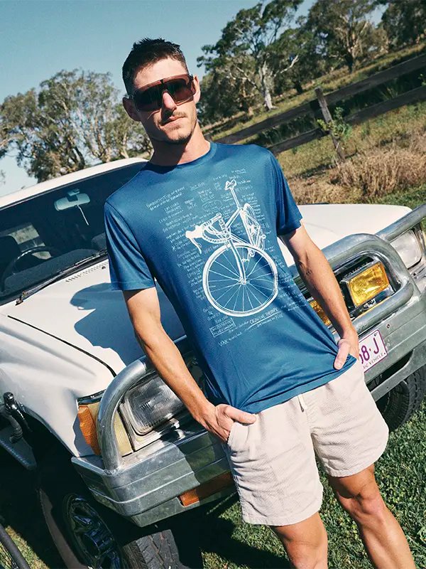 Mann in blauem T-Shirt mit Fahrradmotiv, der neben einem Auto im Freien steht.