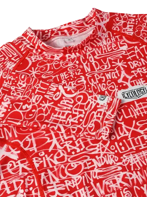 Red cycling jersey with white graffiti-style text design, featuring cycling phrases and brand tag