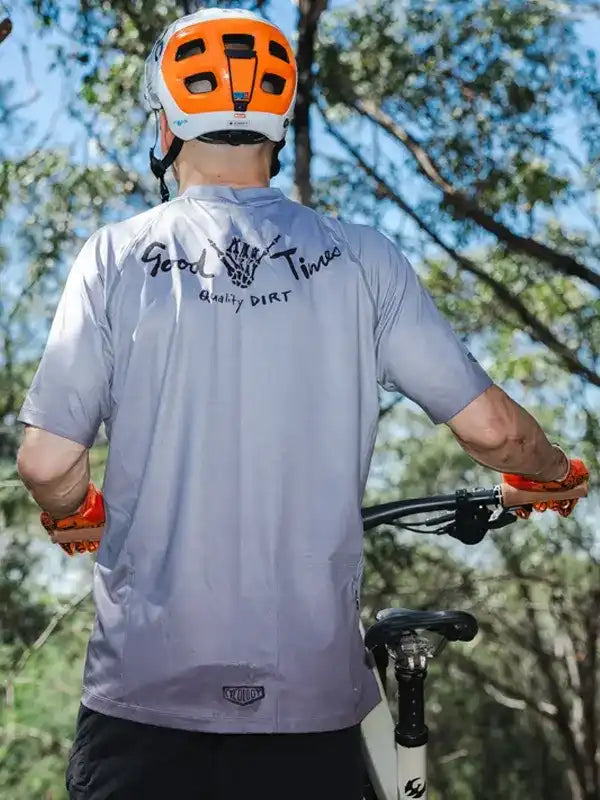 Cyclist wearing gray 'Good Times Quality Dirt' jersey, orange helmet, gloves, on trail bike outdoors