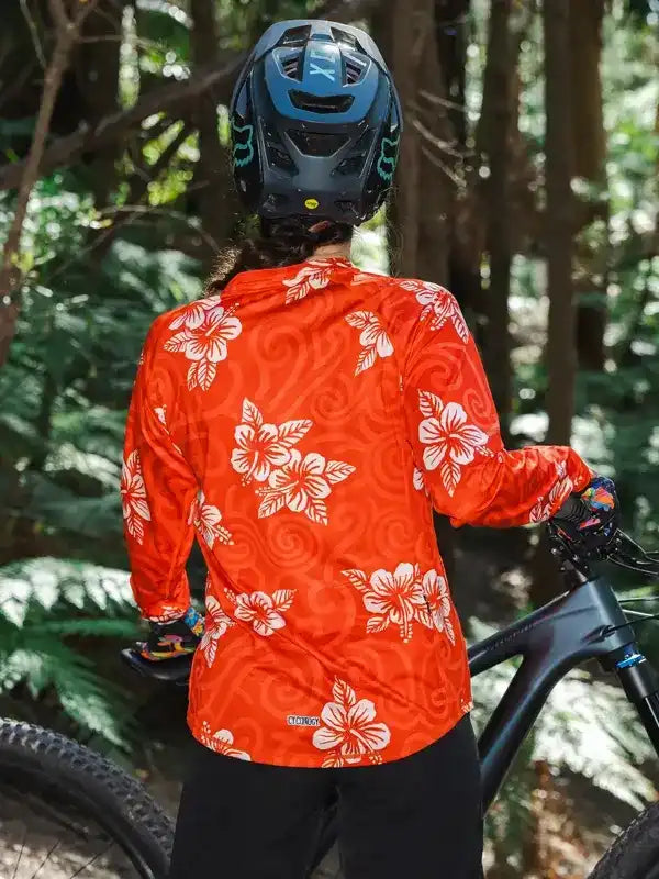 Woman in orange floral cycling jersey and helmet on mountain bike trail