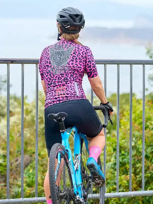 Woman in pink leopard print cycling jersey and black shorts on blue bike, wearing helmet, outdoors