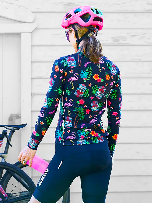 Person wearing a Molokai Black Women's Winter Long Sleeve Cycling Jersey with a helmet, standing next to a bicycle.