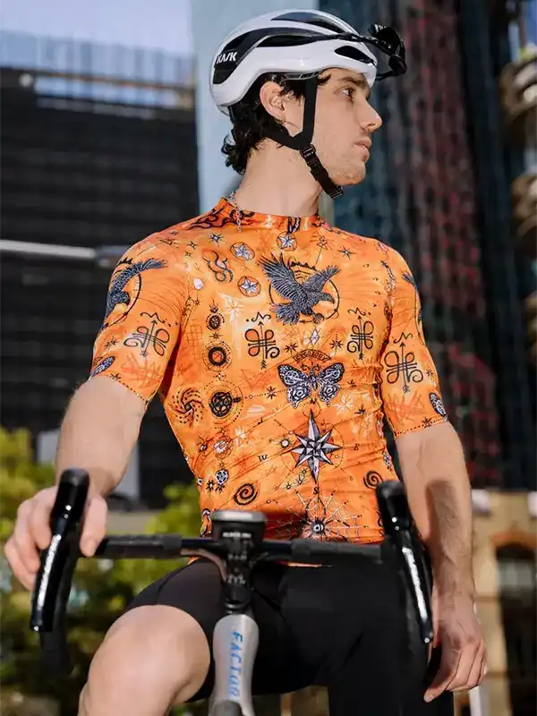 Man cycling in vibrant orange patterned jersey with eagle and butterfly design, wearing helmet, urban backdrop