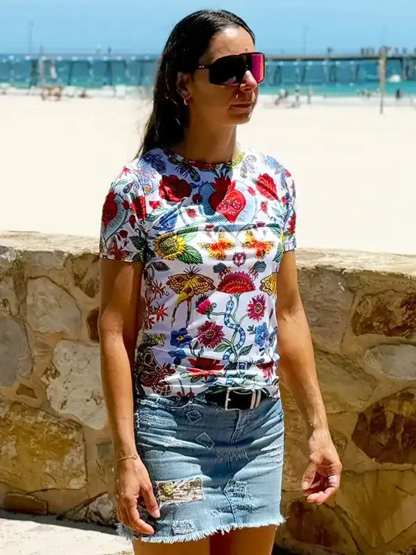 Woman wearing colorful floral print t-shirt and denim skirt at beach, stylish casual summer outfit