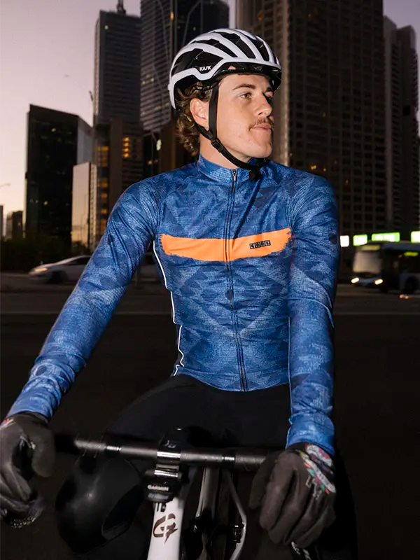 Cyclist in a blue long sleeve cycling jersey  with an orange stripe in an urban setting