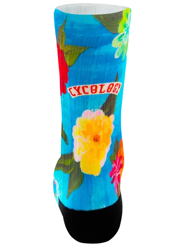 A single crew cycling sock with a bright tropical floral print on a turquoise blue background, featuring orange, red, yellow, and white flowers with green leaves, finished with black toe and heel sections.