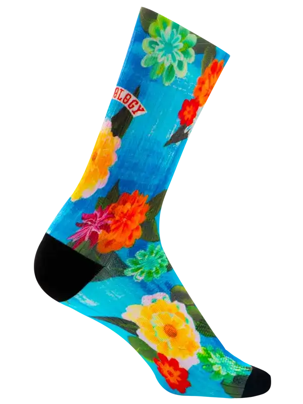 A single crew cycling sock with a bright tropical floral print on a turquoise blue background, featuring orange, red, yellow, and white flowers with green leaves, finished with black toe and heel sections.
