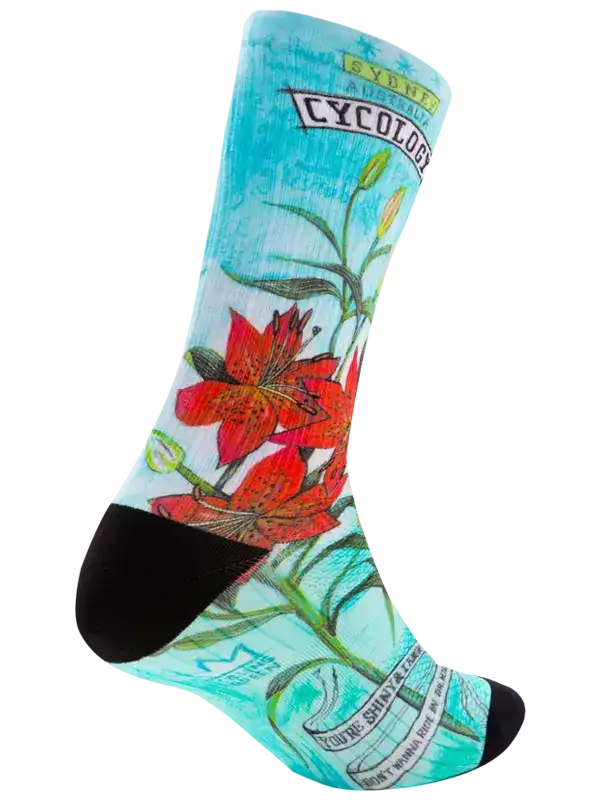A single crew cycling sock with a light blue and white watercolor background, featuring red lily flowers, green stems, and black toe/heel accents. The sock has text graphics including 'CYCOLOGY' and 'The Science of Socks'.