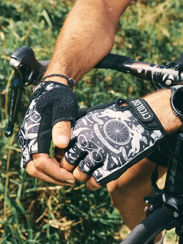 Close-up of a person wearing black and white cycling gloves with a bike design, holding onto a bicycle handlebar.