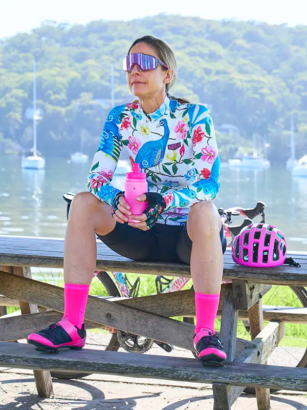 Woman sitting on a picnic table with a scenic background, wearing Goddess White Women's Long Sleeve Summer Cycling Jersey 
