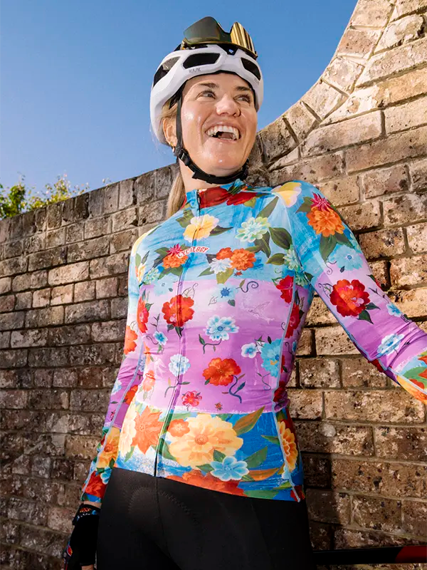 Person wearing a colorful floral long sleeve cycling jersey and helmet against a stone wall.