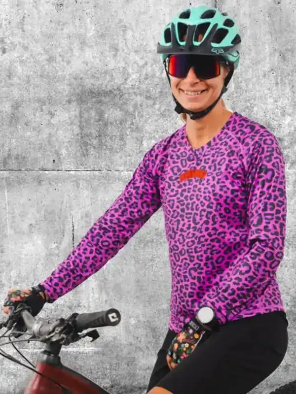 Woman in pink leopard print cycling jersey, helmet, and sunglasses on bike