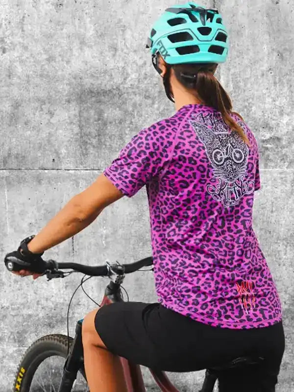 Woman cycling in vibrant pink leopard print jersey with owl graphic, black shorts, and teal helmet