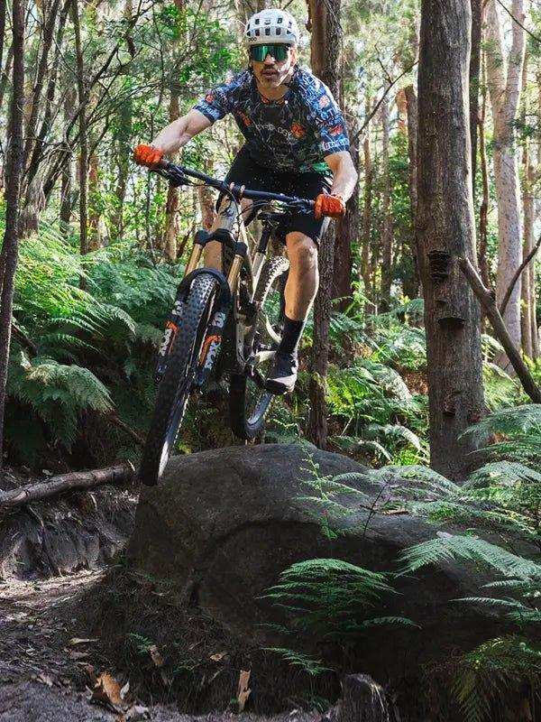 Man mountain biking in forest wearing cycling jersey, helmet, and gloves