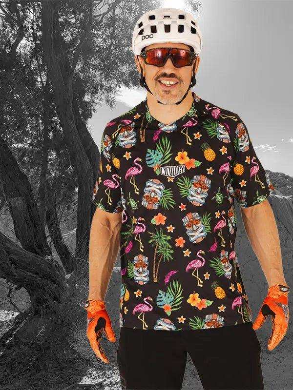 Men's tropical flamingo print cycling jersey with tiki masks, palm leaves, and pineapples, worn with helmet and gloves