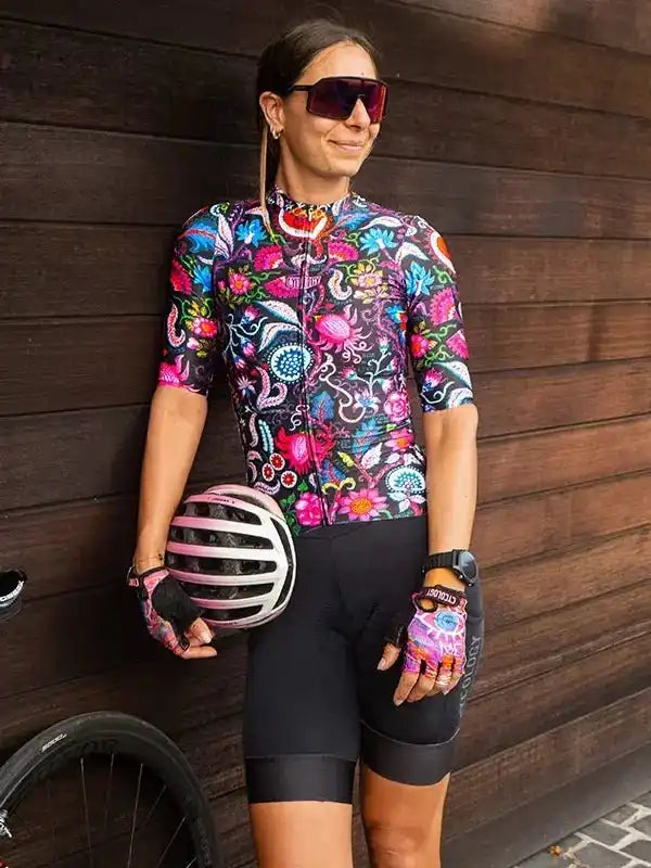 Woman in colorful floral cycling jersey and black shorts, holding helmet, ready for ride