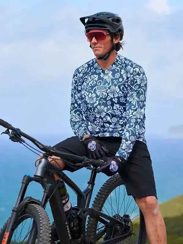 Man in floral cycling jersey and helmet on mountain bike overlooking ocean, wearing sunglasses and gloves