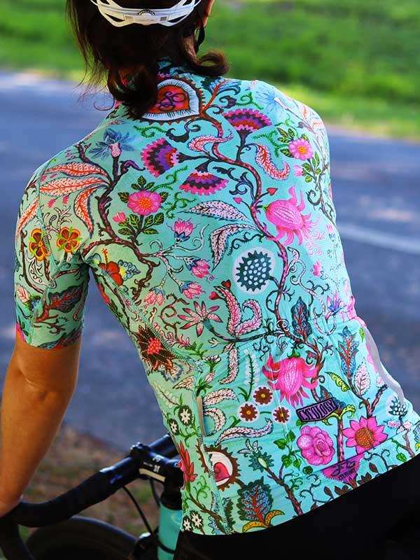 Woman cycling in vibrant floral patterned jersey, ideal for road rides and outdoor adventures.