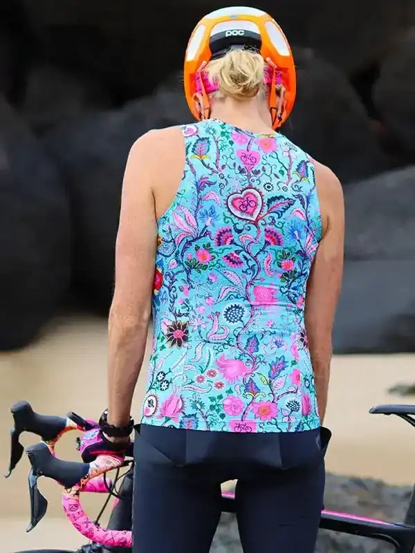 Woman in colorful floral cycling jersey and orange helmet, standing with road bike outdoors